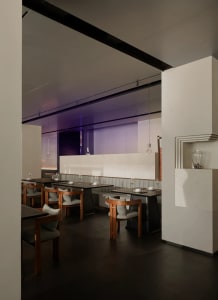 A modern restaurant with a large dining area featuring tables, chairs, and wine glasses, creating an inviting atmosphere for socializing and dining