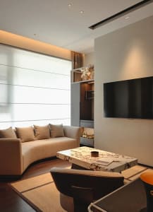 Modern living room with a large couch, flat screen TV, two chairs, and a dining table in a clean and bright space with white walls