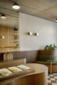 Modern restaurant interior with a counter, dining table, chairs, potted plants, and cups, featuring a welcoming atmosphere