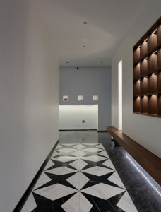 A clean and organized hotel lobby with a black and white checkered tile floor, two benches, and three clocks on the wall