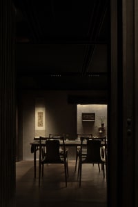 Dimly lit dining area with a wooden table, multiple chairs, and a vase, creating a cozy ambiance