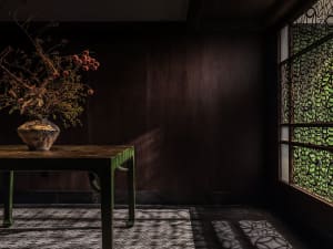 Cozy living room with a wooden table, brown walls, and a vase of flowers, featuring two chairs and a warm atmosphere