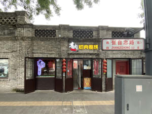 A warm and inviting Asian restaurant with a brick exterior, wooden doors, and red accents, featuring tables and chairs arranged in a comfortable dining atmosphere