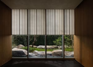 A living area with a large window offering a view of a garden, surrounded by potted plants and natural light