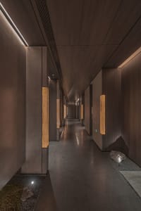 A calm and inviting empty hallway with a wooden floor and ample lighting from multiple fixtures on both sides