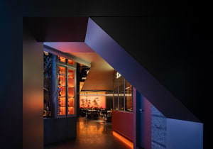 A cozy bar area with a dining table surrounded by chairs, bottles on surfaces, and an inviting atmosphere for socializing and enjoying food and drinks