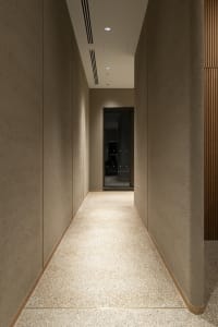 Dark office hallway with a carpeted floor, concrete walls, and an empty space leading to another room