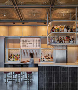 A modern bar with a counter and seating area, featuring bottles and wine glasses, creating a social and inviting atmosphere