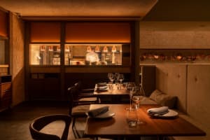 Warm and inviting restaurant interior with wooden tables, chairs, and soft lighting, featuring wine glasses and a cozy ambiance