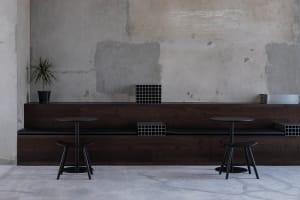 A restaurant interior with a wooden dining table, black chairs, and brick-patterned walls, creating a stylish and comfortable atmosphere for dining and socializing