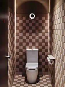 Small bathroom with a white toilet, brown tile walls, and a sink in the background