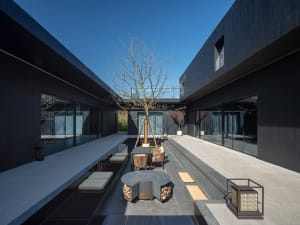 Modern house with a black exterior, large windows, chairs, and a dining table, creating a comfortable and inviting atmosphere