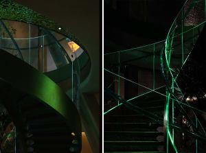 A modern staircase with metal steps in green and black, set against a neutral background