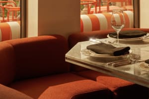 A cozy dining area with an orange couch, chairs, wine glasses, and knives on a table, creating a warm and inviting atmosphere