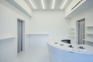 A minimalist kitchen dining space with white surfaces, a large counter, and a sink and refrigerator, giving off a clean and bright atmosphere