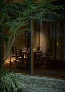 Dining area with a large wooden table, chairs, and wine glasses, set up for a formal dinner with natural light from windows