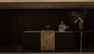 A casual cafe interior with a wooden counter, a coffee maker, and a woman standing behind it