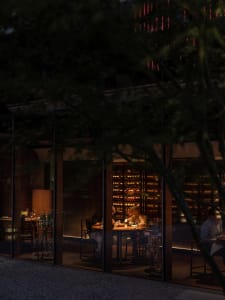 A cozy indoor dining area with wooden tables and chairs, set with wine glasses, cups, and other dining items, under dimly lit ambiance