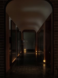 A dark hallway with a black tile floor, featuring two people standing at the end, with no windows or natural light