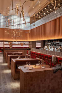 Warm and inviting restaurant interior with wooden floors and walls, featuring dining tables, chairs, wine glasses, and bottles in a comfortable and welcoming environment