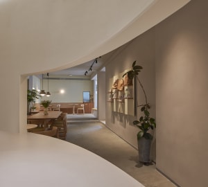 A cozy cafe with a curved wall, chairs, dining tables, potted plants, and decorative elements
