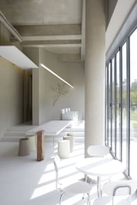 A spacious dining area with a large white table surrounded by chairs, concrete elements, and natural light from windows