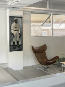Cozy living space with a large painting of a baseball player, a brown leather chair, a smaller chair, and a potted plant, creating a warm and inviting atmosphere