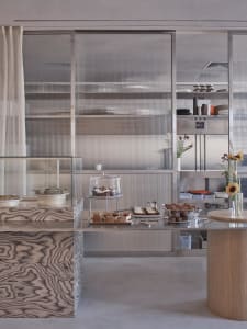 Modern restaurant kitchen with stainless steel appliances and surfaces, a counter with displayed food items, and a contemporary atmosphere