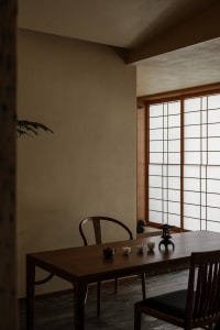A dining area with a wooden table and chairs, surrounded by natural light from a window, creating a warm and inviting atmosphere