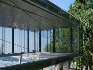 Exterior photo of a modern building with a glass facade, multiple windows, and a natural background with trees
