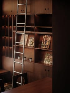 A darkened room with a wooden bookshelf filled with books and two cups on the lower shelves, creating a cozy and inviting atmosphere