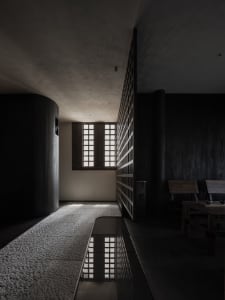 Dimly lit hallway with a wooden door, two chairs, and a dining table, creating a cozy and mysterious atmosphere