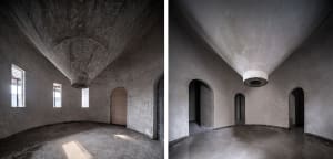 A large, empty room with a vaulted ceiling, arches, and a stone wall, showcasing a minimalist space with no furniture or objects
