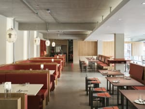 Empty restaurant interior with red benches, wooden tables, and metal elements, featuring warm lighting and a modern design