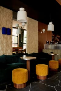 Cozy cafe interior with yellow and green couches, tables, chairs, and lamps, featuring potted plants and vases, with a warm and inviting atmosphere
