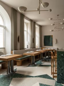 Modern restaurant interior with concrete walls, multiple tables, benches, and hanging lamps creating a warm atmosphere