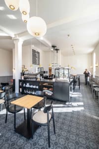 Inviting restaurant interior with wooden accents, multiple tables, chairs, and a bar counter, featuring bottles and a warm atmosphere