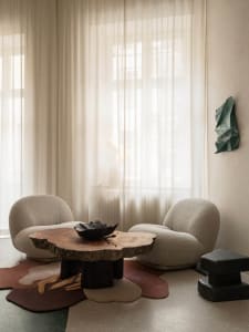 A warm and inviting living area with two white chairs, a rug, and a table, featuring a bowl of decoration, set against a neutral color palette and soft lighting