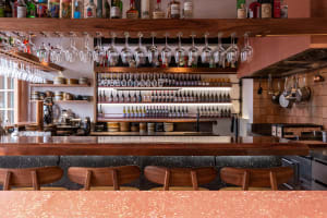 A cozy bar area with a wooden countertop, wine bottles, and comfortable seating for patrons