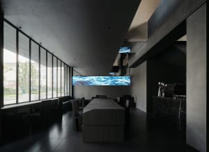 Modern restaurant with a large screen displaying water flowing down a river, surrounded by chairs and tables