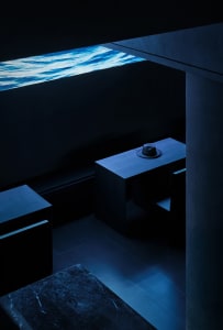 Dark room with a black table and chair in front of an aqua-tinted window, two chairs on either side of the table