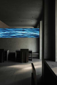 Modern dining space with two tables and chairs, minimalist aesthetic, and a large screen on the wall