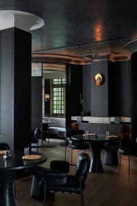 Modern restaurant interior with multiple tables, chairs, potted plants, and warm lighting