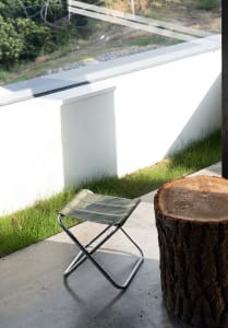 A well-lit outdoor patio with a green chair and a tree stump, surrounded by a relaxing atmosphere