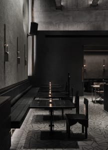 Empty modern restaurant with black walls, dining tables, and candles creating a warm atmosphere