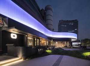 A modern office building at night with a large glass structure and curved design, featuring several windows on its facade