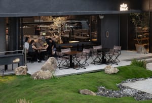 An outdoor dining area with several tables and chairs, surrounded by potted plants, creating a comfortable and inviting atmosphere for socializing and enjoying meals in an open-air setting