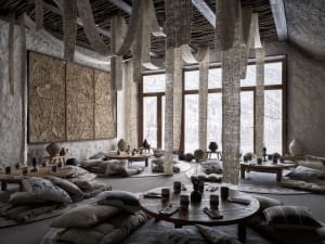 A warm and inviting dining space with a wooden ceiling, stone walls, and a round table surrounded by chairs, with vases placed throughout the space