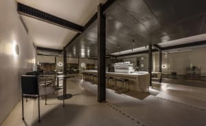 Industrial kitchen with a modern design, featuring a large countertop island, multiple dining tables, and chairs, in a clean and well-organized atmosphere