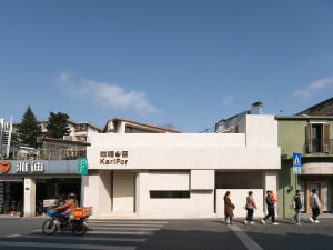 A busy city street scene with a white building, pedestrians, and a person on a bicycle